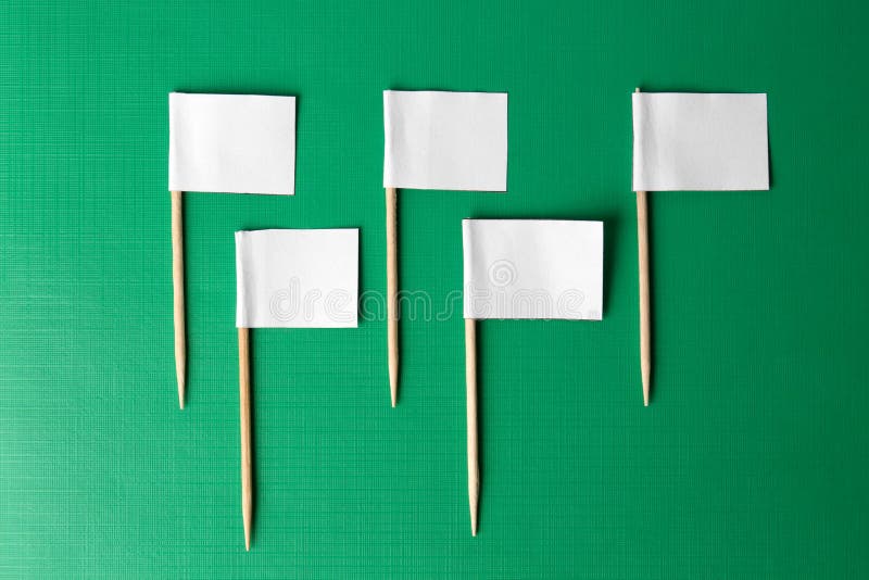 Many white paper flags on green background, flat lay stock image