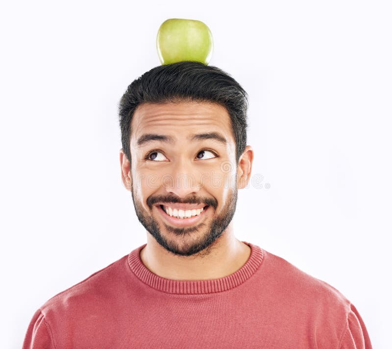 Manzana feliz y equilibrio en la cabeza con un hombre en estudio aislado en un fondo blanco para dieta o nutrición. sonrisa