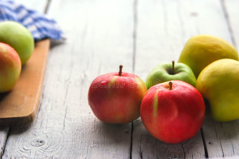 Manzanas en un primer de madera blanco de la tabla. La instalación da fruto comida amarilla verde fresca