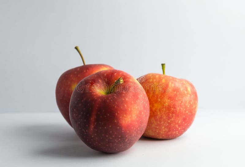 A still life style photograph of a set of three vibrantly red orange and yellow apples upon an isolated and white background. A still life style photograph of a set of three vibrantly red orange and yellow apples upon an isolated and white background.