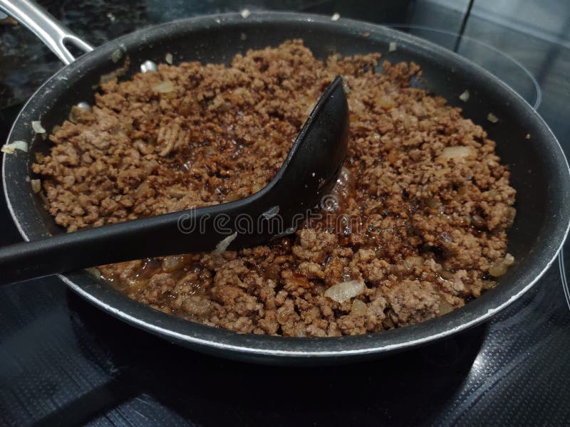 A plastic ladle rests on top of browned beef in a steel skillet. A plastic ladle rests on top of browned beef in a steel skillet.