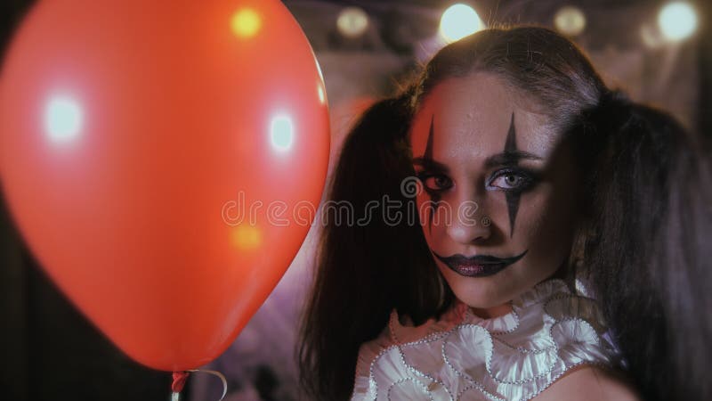 Easy Halloween Makeup. Girl with a red balloon, in the form of a clown. On black background. The ball disappears and reappears. Easy Halloween Makeup. Girl with a red balloon, in the form of a clown. On black background. The ball disappears and reappears