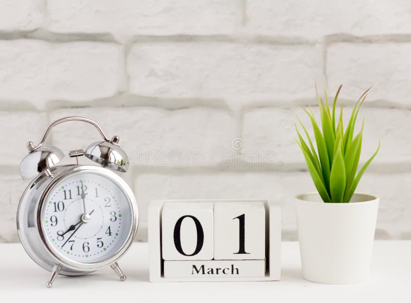march-1-on-a-wooden-calendar-next-to-an-alarm-clock-and-a-flower-on-a-white-background-the