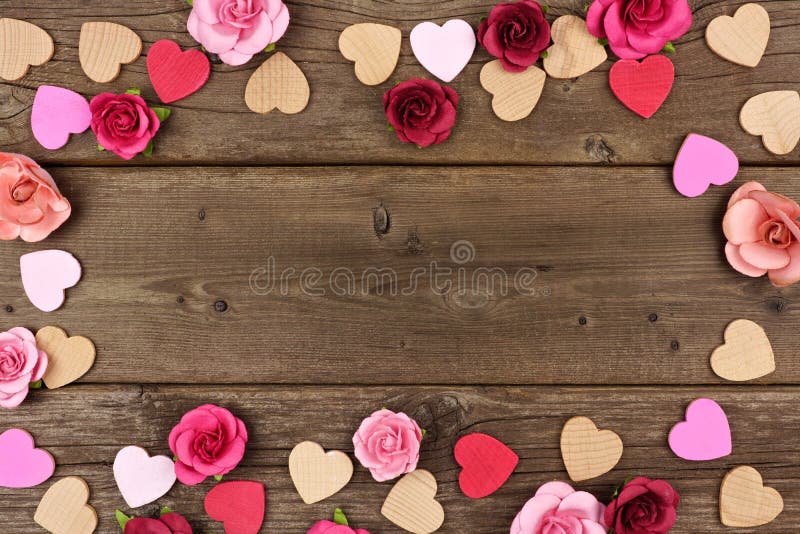 Valentines Day frame of wooden hearts and paper roses against a rustic wood background with copy space. Valentines Day frame of wooden hearts and paper roses against a rustic wood background with copy space.