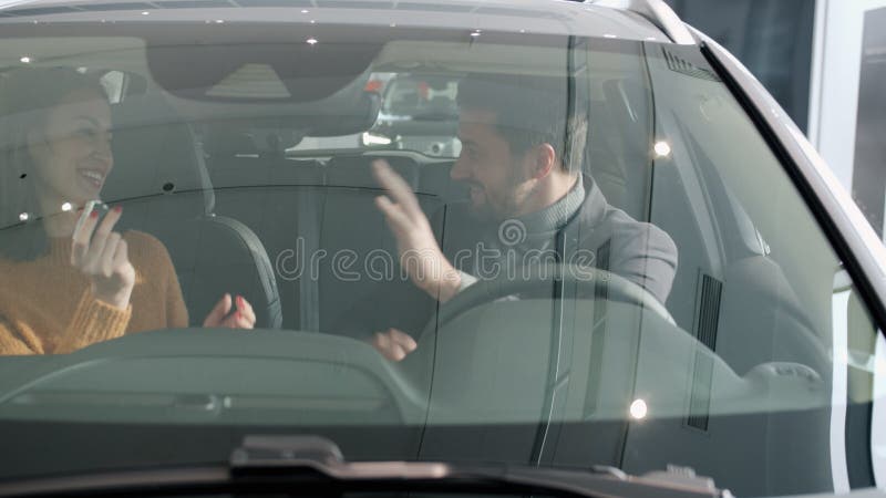 Marido amante dando llaves de auto a la esposa feliz sentada dentro de un nuevo automóvil
