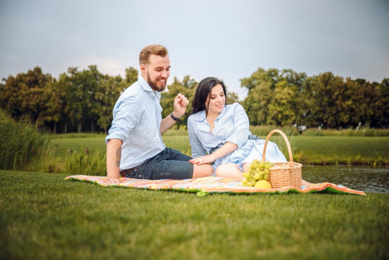 Marido novo alegre feliz da família e sua esposa grávida que têm o divertimento junto fora, no piquenique no parque do verão imagem de stock Marido novo alegre feliz da família e sua esposa grávida que têm o divertimento junto fora, no piquenique no parque do verão imagem de stock
