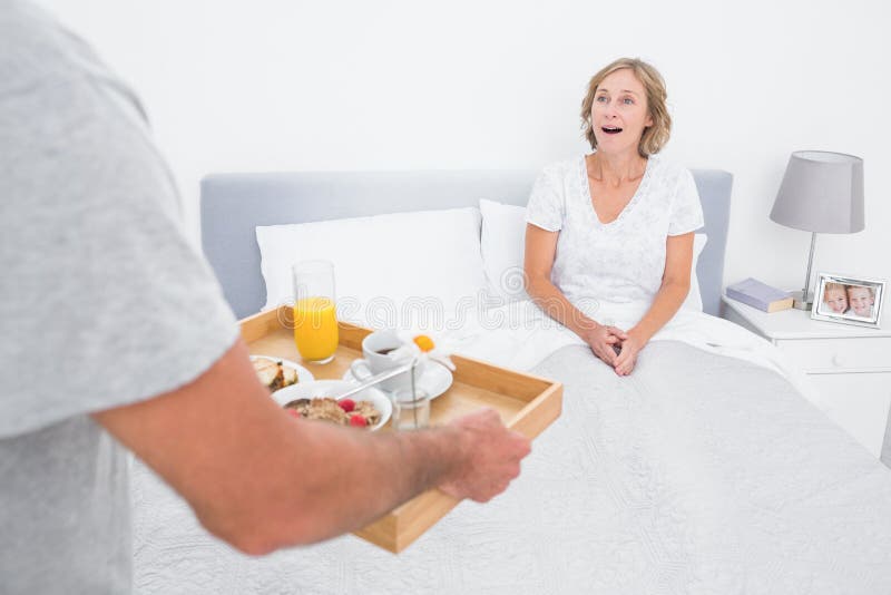 Marido que trae el desayuno en cama a la esposa sorprendida fotografía de archivo libre de regalías Marido que trae el desayuno en cama a la esposa sorprendida fotografía de archivo libre de regalías