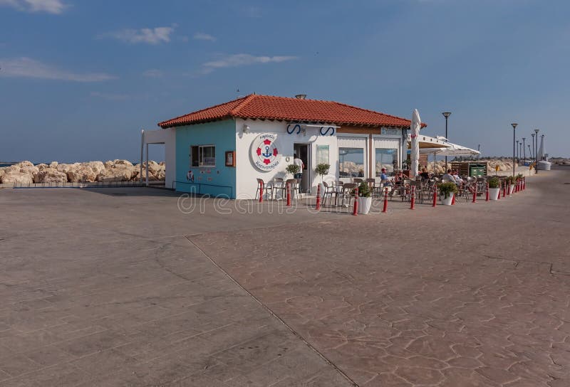Marina Cafe in Zygi op de dag van de heldere zonnige winter Mensen die uit bij lijsten en stoelen zitten die van het mooie weer g stock afbeelding Marina Cafe in Zygi op de dag van de heldere zonnige winter Mensen die uit bij lijsten en stoelen zitten die van het mooie weer g stock afbeelding