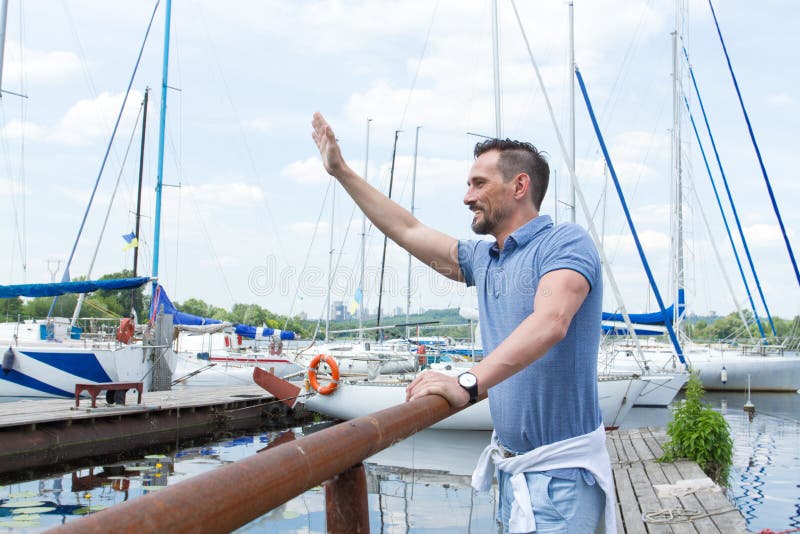 Marinheiro masculino que acena acima no cais e no sorriso O 'yachtsman' dá o comando amarrar à mão na doca Boas vindas do homem q imagens de stock Marinheiro masculino que acena acima no cais e no sorriso O 'yachtsman' dá o comando amarrar à mão na doca Boas vindas do homem q imagens de stock