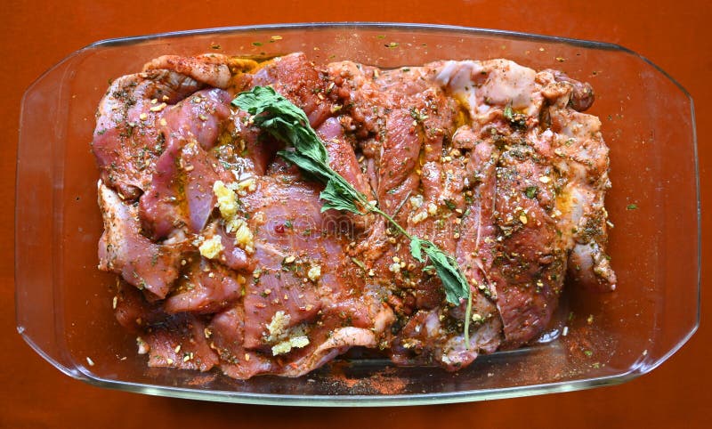 Mariniertes Fleisch mit Kräutern und Gewürzen in einer Glasschale, bereit zum Kochen an einer Küchentheke lizenzfreies stockbild