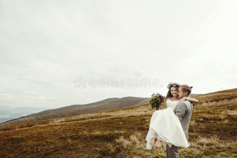 Marié élégant portant la jeune mariée heureuse et ayant l'amusement, mariage de boho photos stock Marié élégant portant la jeune mariée heureuse et ayant l'amusement, mariage de boho photos stock