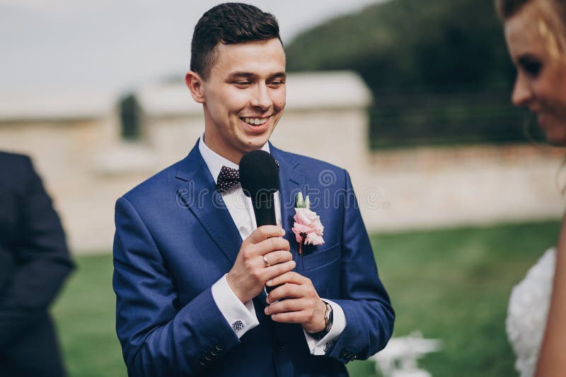 Marié élégant prononçant le voeu à sa belle jeune mariée pendant le mariage Marié prononçant la parole et tenant le microphone Be image libre de droits Marié élégant prononçant le voeu à sa belle jeune mariée pendant le mariage Marié prononçant la parole et tenant le microphone Be image libre de droits