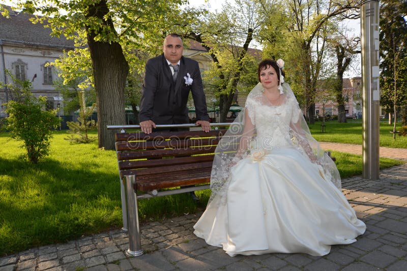 Bride and groom in the park. A women sits on a bench, a men rests his hands on the back of the bench. Silk dress champagne color. A suit with a white flower in your pocket. White flower in the hair, background, beautiful, beauty, ceremony, city, costume, couple, day, expectation, face, family, female, flared, skirt, future, girl, happiness, happy, husband, jacket, love, marriage, marry, nature, relationship, romance, romantic, scarf, shoulder, smile, summer, together, touch, two, wedding, wife, young, people, green. Bride and groom in the park. A women sits on a bench, a men rests his hands on the back of the bench. Silk dress champagne color. A suit with a white flower in your pocket. White flower in the hair, background, beautiful, beauty, ceremony, city, costume, couple, day, expectation, face, family, female, flared, skirt, future, girl, happiness, happy, husband, jacket, love, marriage, marry, nature, relationship, romance, romantic, scarf, shoulder, smile, summer, together, touch, two, wedding, wife, young, people, green