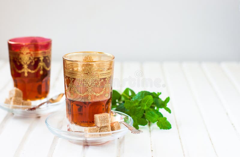 Marokkanischer Tee mit Minze und Zucker in einem Glas auf einer weißen Tabelle mit einem Kessel lizenzfreie stockfotografie Marokkanischer Tee mit Minze und Zucker in einem Glas auf einer weißen Tabelle mit einem Kessel lizenzfreie stockfotografie