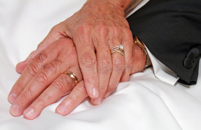 Marriage. The left hand of a wife holding her husband's, both wearing wedding rings, both hands show aging. A concept of lasting marriage royalty free stock photography