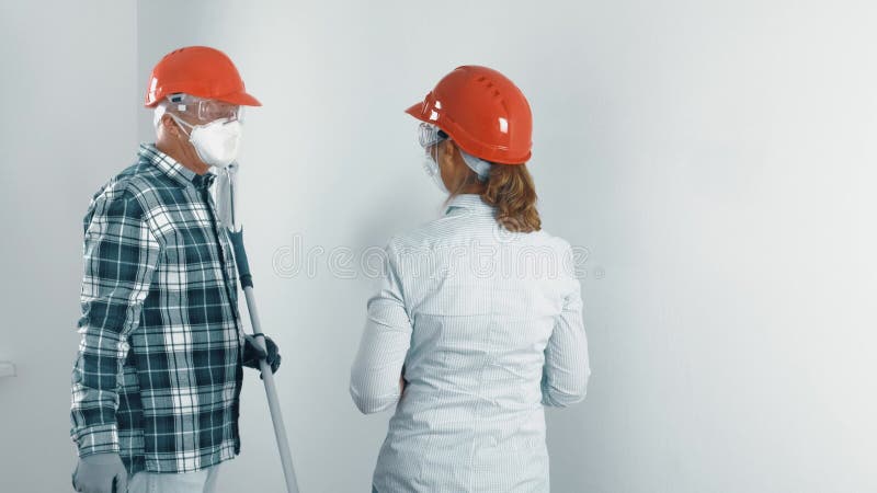 An elderly married couple, a man with a beard and a woman in protective masks and helmets are repairing an apartment.