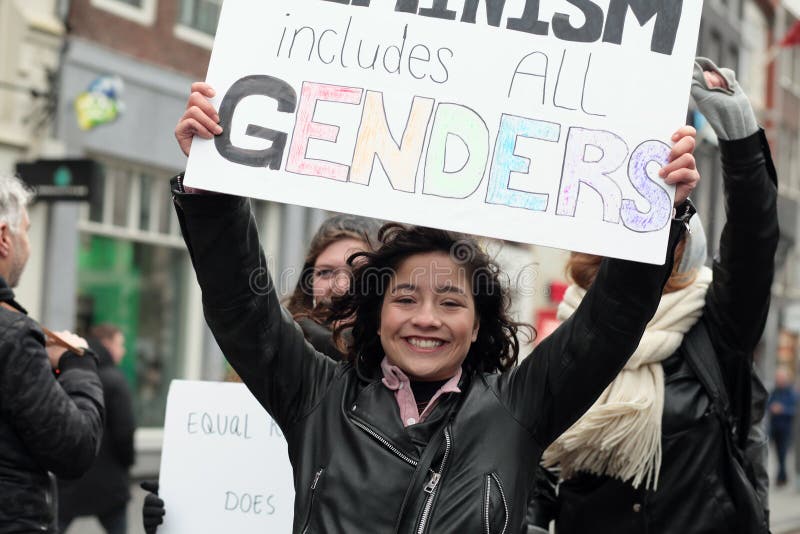 Amsterdam / Netherlands - March 8 2020: Woman marching and holding a sign saying Feminism includes all gender. Amsterdam / Netherlands - March 8 2020: Woman marching and holding a sign saying Feminism includes all gender