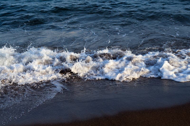 Maré espumosa da água do mar na praia vulcânica escura Ressaca de relaxamento da onda do mar sobre o litoral imagens de stock Maré espumosa da água do mar na praia vulcânica escura Ressaca de relaxamento da onda do mar sobre o litoral imagens de stock