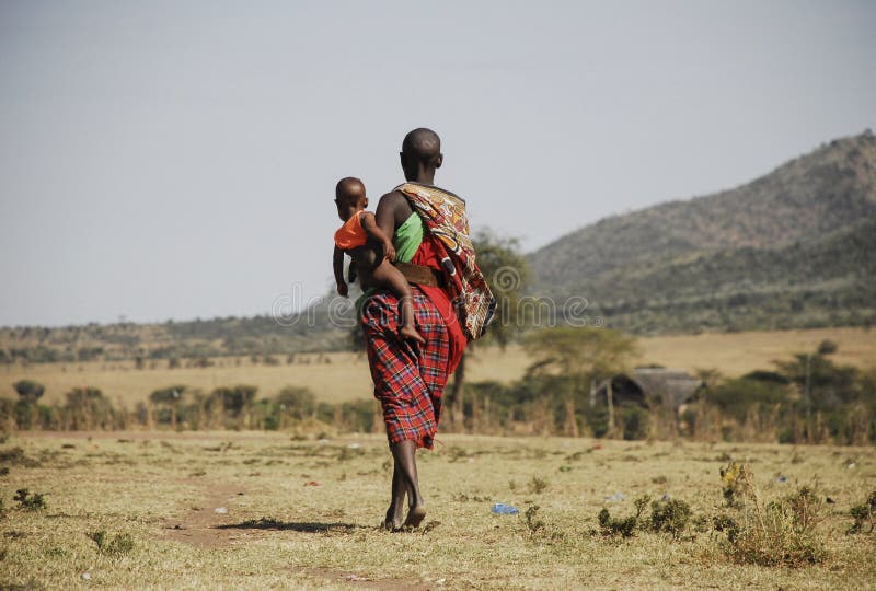 Masai Mara, Quênia - 4 de setembro de 2006: Mulher tribal Masai carregando seu bebê andando pela savana fotos de stock royalty free Masai Mara, Quênia - 4 de setembro de 2006: Mulher tribal Masai carregando seu bebê andando pela savana fotos de stock royalty free