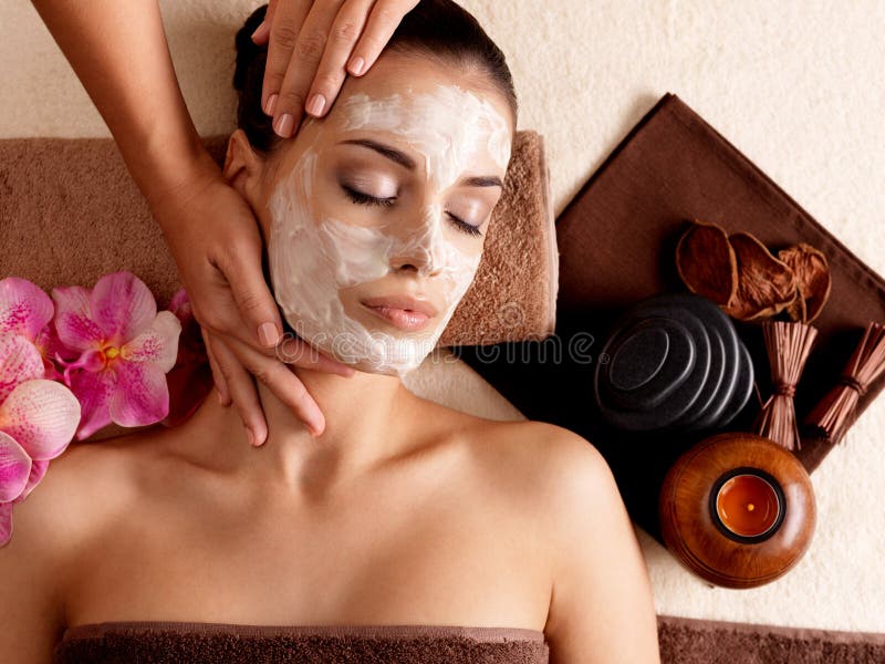 Masaje del balneario para la mujer con la máscara facial en cara