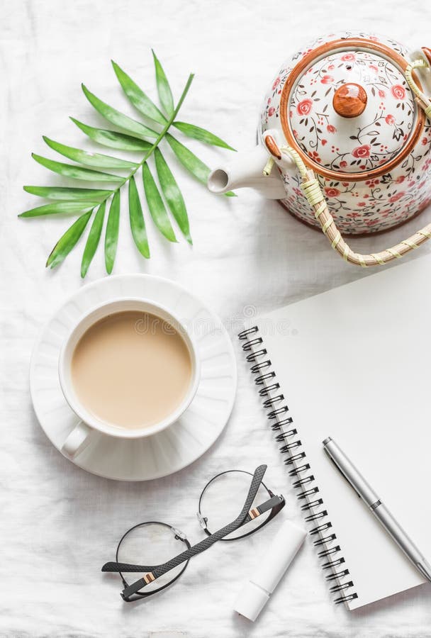 Masala tea, teapot, notepad, glasses, pen, green flower leaf on white background, top view. Morning inspiration planning.