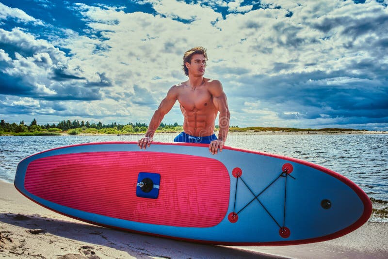 Maschio del surfista con un corpo muscolare con il suo surf alla spiaggia fotografia stock libera da diritti Maschio del surfista con un corpo muscolare con il suo surf alla spiaggia fotografia stock libera da diritti