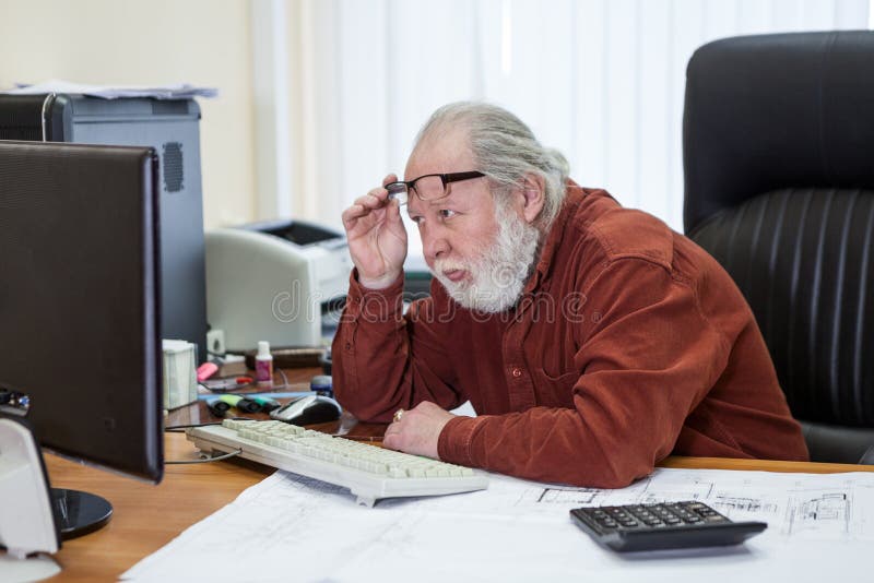 Maschio dell'uomo senior che si siede allo scrittorio che porta una camicia, avendo difficoltà o problemi per mezzo di un compute fotografia stock libera da diritti Maschio dell'uomo senior che si siede allo scrittorio che porta una camicia, avendo difficoltà o problemi per mezzo di un compute fotografia stock libera da diritti