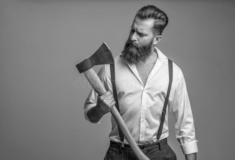 Masculinalità dell'uomo barbuto con un'ascia isolata in grigio. uomo brutale caucasico con barba e baffi. Energia maschile fotografia stock