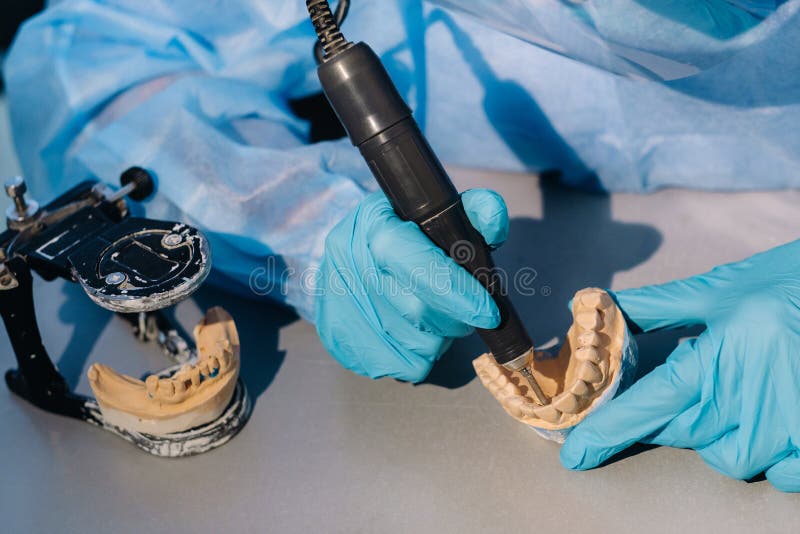 A Masked and Gloved Dental Technician Works on a Prosthetic Tooth in