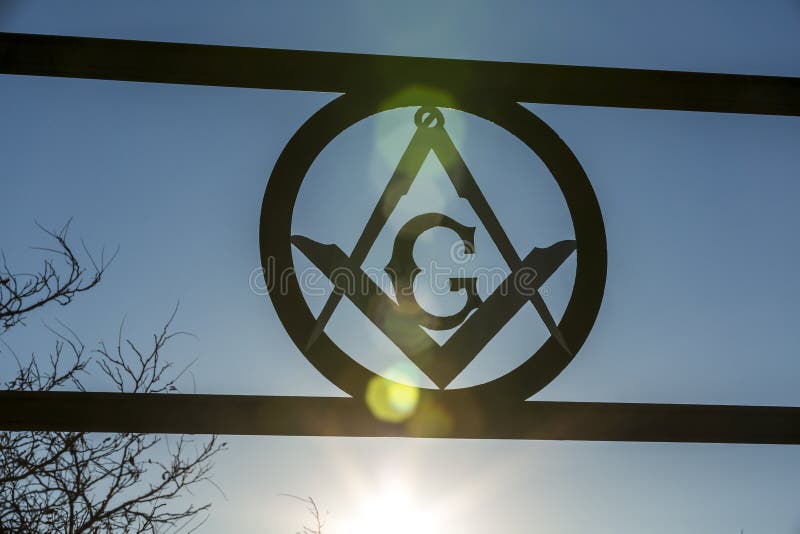 Masonic square and compass sign backlit against a blue sky with sunflare