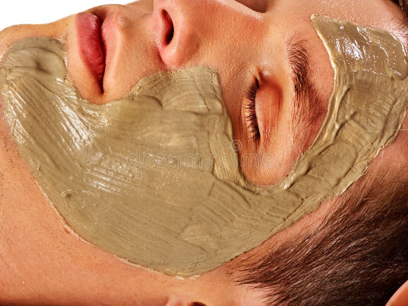 Mud facial mask of man in spa salon. Massage with clay full face. Close up man lying on spa bed on therapeutic procedure . Cropped shot of home cosmetics with egg yolk. Mud facial mask of man in spa salon. Massage with clay full face. Close up man lying on spa bed on therapeutic procedure . Cropped shot of home cosmetics with egg yolk.