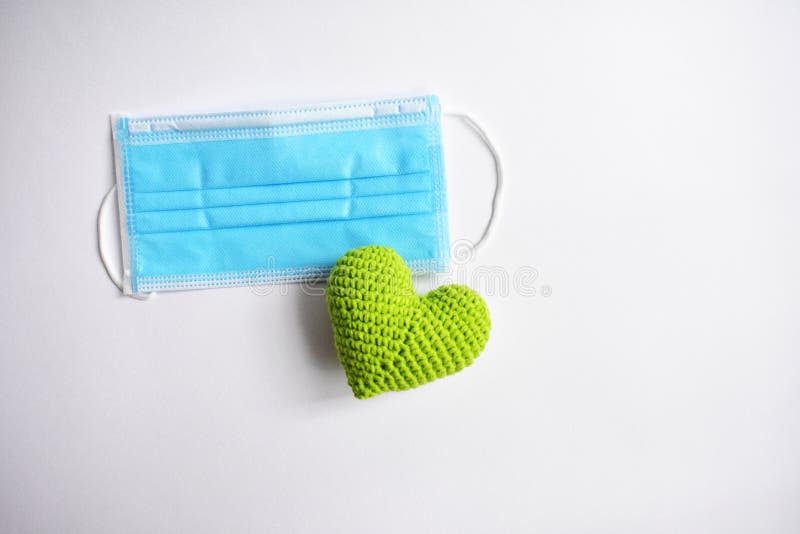 Medical face mask in white background, green crochet heart and protective mask for spreading of disease virus CoV-2 Corona virus Disease 2019 quarantine, stay safe, hospital. Medical face mask in white background, green crochet heart and protective mask for spreading of disease virus CoV-2 Corona virus Disease 2019 quarantine, stay safe, hospital