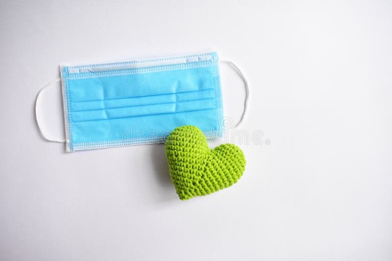 Medical face mask in white background, green crochet heart and protective mask for spreading of disease virus CoV-2 Corona virus Disease 2019 quarantine, stay safe, hospital. Medical face mask in white background, green crochet heart and protective mask for spreading of disease virus CoV-2 Corona virus Disease 2019 quarantine, stay safe, hospital