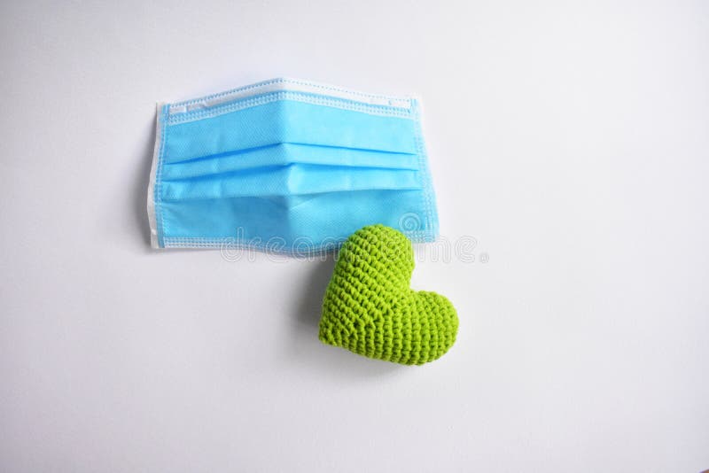 Medical face mask in white background, green crochet heart and protective mask for spreading of disease virus CoV-2 Corona virus Disease 2019 quarantine, stay safe, hospital. Medical face mask in white background, green crochet heart and protective mask for spreading of disease virus CoV-2 Corona virus Disease 2019 quarantine, stay safe, hospital