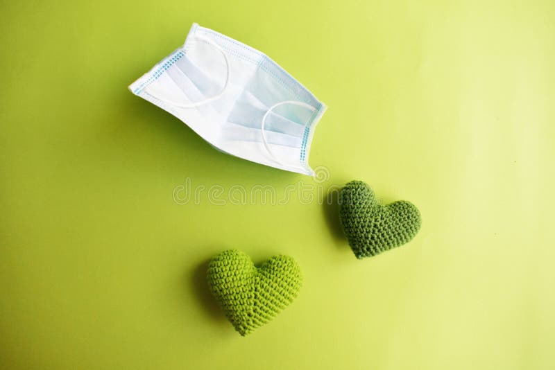 Medical face mask in green background, green crochet heart and protective mask for spreading of disease virus CoV-2 Corona virus. Medical face mask in green background, green crochet heart and protective mask for spreading of disease virus CoV-2 Corona virus