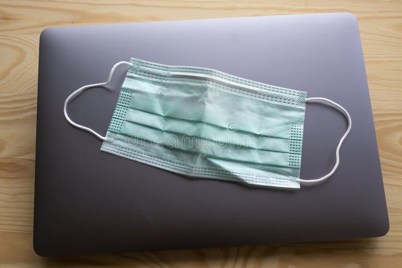 Face mask, Medical mask, Surgical mask on laptop,  Wooden texture background, Close up shot, Selective focus, Prevention from covid19, Coronavirus, Bacteria, Healthcare. Face mask, Medical mask, Surgical mask on laptop,  Wooden texture background, Close up shot, Selective focus, Prevention from covid19, Coronavirus, Bacteria, Healthcare