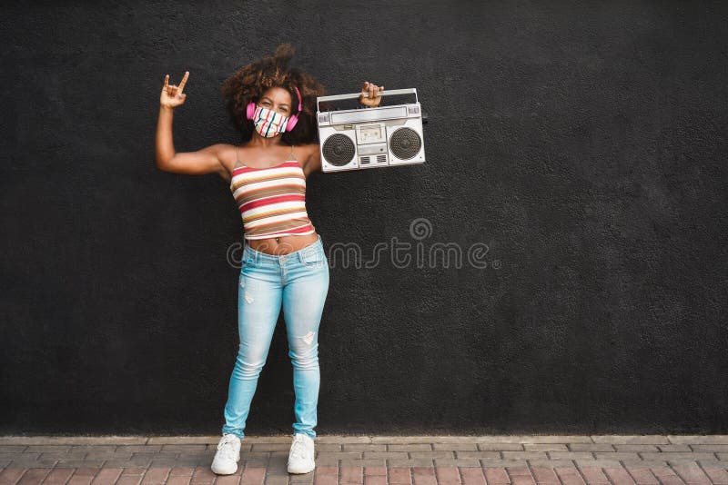 Happy black woman wearing face protective mask having fun and dancing while holding a retro radio. Happy black woman wearing face protective mask having fun and dancing while holding a retro radio