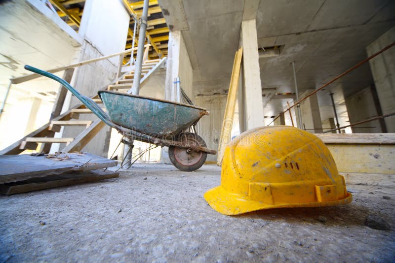 Yellow hard hats and small cart on concrete floor inside unfinished building. Yellow hard hats and small cart on concrete floor inside unfinished building