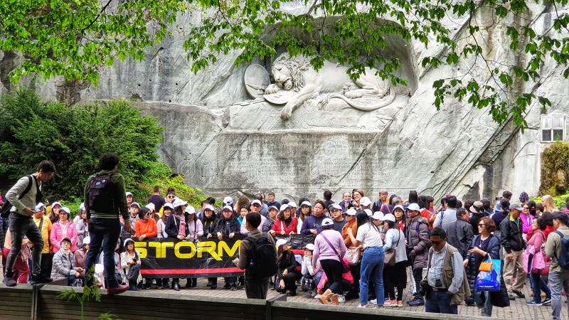 Mass tourists taking a group picture in front of Lion monument, Lucerne Switzerland. The Lion Monument in Lucerne is a giant dying lion carved out of a wall of sandstone rock above a pond at the east end of the medieval town. It was designed as a memorial for the mercenary soldiers from central Switzerland who lost their lives while serving the French king Louis XVI during the French Revolution