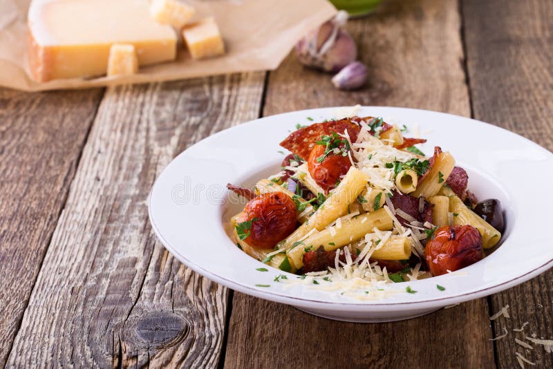 Massa de Rigatoni com salame, os tomates de cereja roasted, e as azeitonas imagem de stock Massa de Rigatoni com salame, os tomates de cereja roasted, e as azeitonas imagem de stock