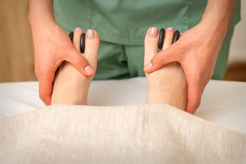 Massager Doing Feet and Toes Massage with Rocks between a Female Toes