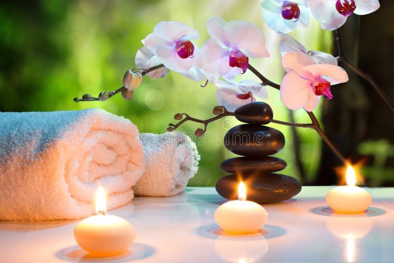 Massaggi la stazione termale della composizione con le candele, le orchidee e le pietre nere in giardino Massaggi la stazione termale della composizione con le candele, le orchidee e le pietre nere in giardino
