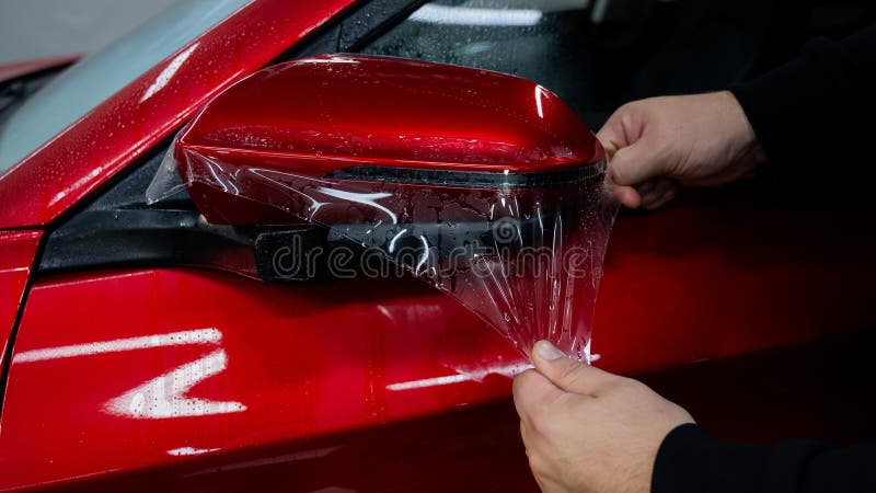 The master applies vinyl film to the side view mirror of a car. stock images
