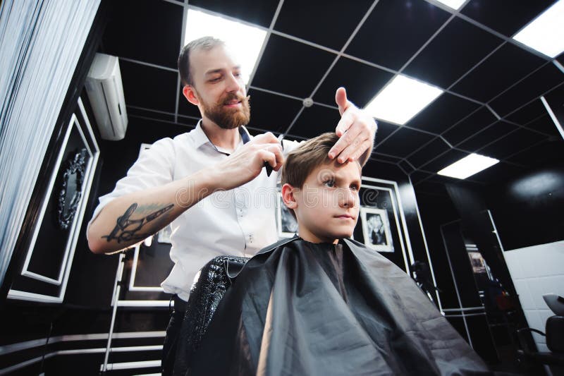 Master cuts hair of a boy in the barbershop, hairdresser makes hairstyle for a boy stock image Master cuts hair of a boy in the barbershop, hairdresser makes hairstyle for a boy stock image