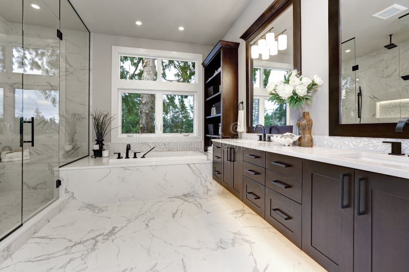 Master modern bathroom interior in luxury home with dark hardwood cabinets, white tub and glass door shower