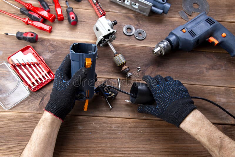 The master repairs a broken electrical device: drill, cutter on a wooden table. Electric Tool Repair Shop royalty free stock image The master repairs a broken electrical device: drill, cutter on a wooden table. Electric Tool Repair Shop royalty free stock image