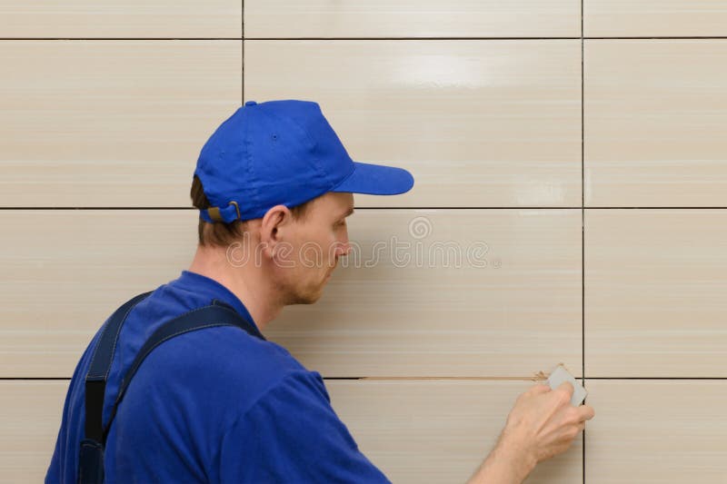 Master-tiler blocks the seams between the tiles with beige cement grout stock photo
