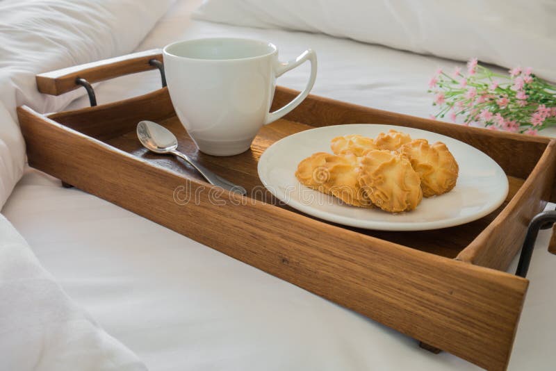 Masło filiżanka w drewnianej tacy na wygodnym łóżku i ciastka