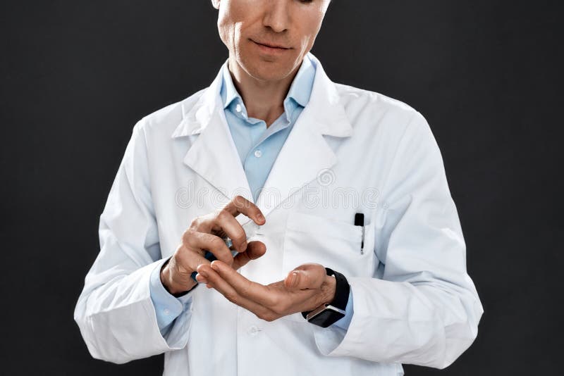 Matando coronavírus. Foto cortada de um médico macho maduro de uniforme médico usando sanitizer, ao mesmo tempo que se opunha fotos de stock