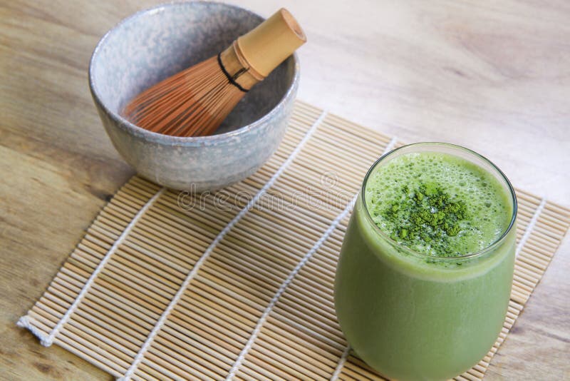 Matcha Green Tea Smoothie with Stone Bowl and wooden whisk on bamboo mat on table